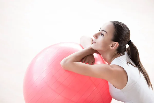 Pensive beautiful woman resting her hands on a fitness ball