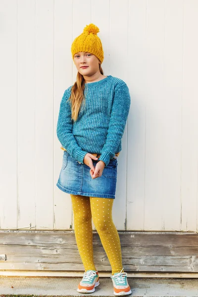 Outdoor fashion portrait of cute 9 year old little girl, wearing yellow hat, blue pullover, denim skirt and polka dot tights