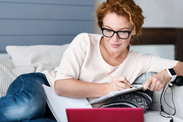 Woman on couch with laptop making notes