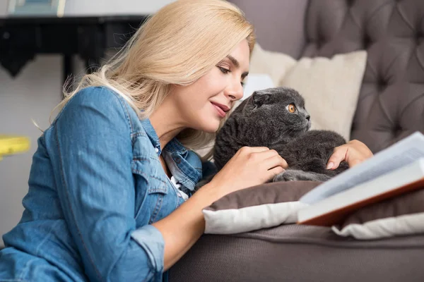 Pretty blond woman reading book with her cat