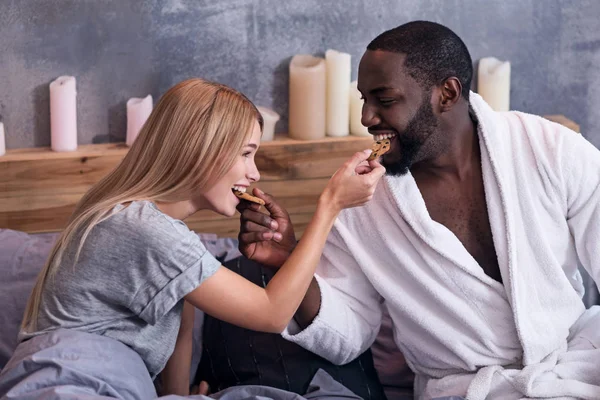 Sweet couple feeding each other with cookies in bed