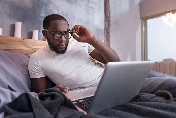 African man using laptop in bedroom