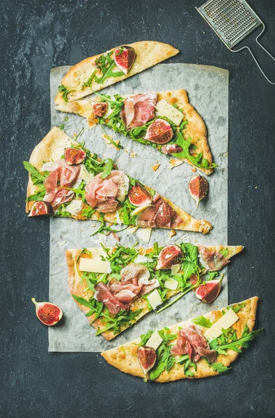 Fig, prosciutto, arugula and sage flatbread pizza on dark background