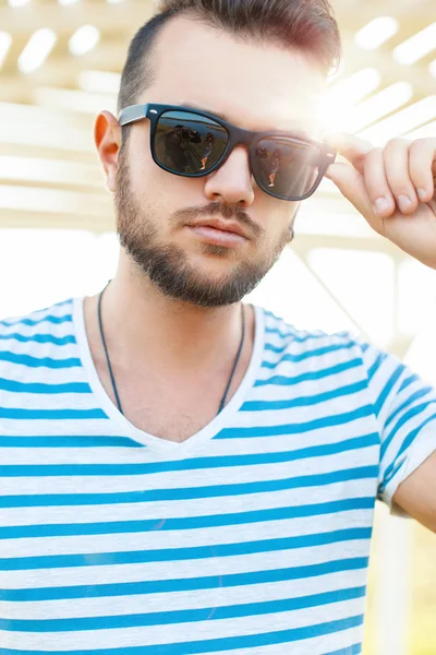 Handsome hipster guy with a beard and with sunglasses in the sunlight on the beach on a summer day.