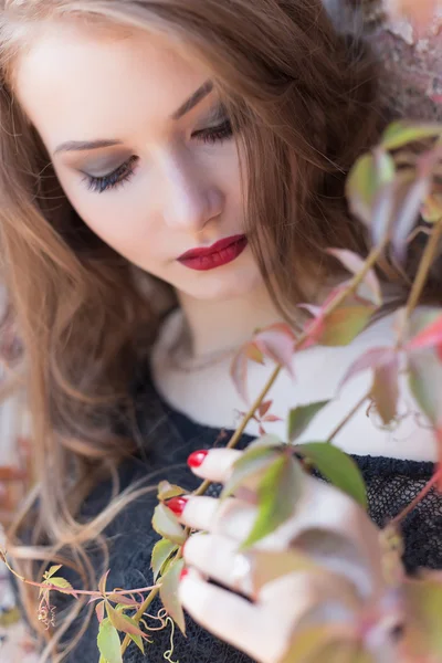 Autumn portrait of a beautiful woman with red hair with bright red lipstick on her lips in the city among the bright colored leaves on a sunny bright day