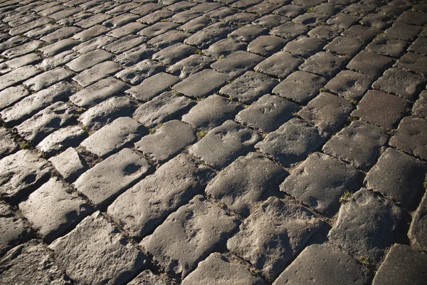 Black cobbled stone road background with reflection of light seen on the road. Black or dark grey stone pavement texture.