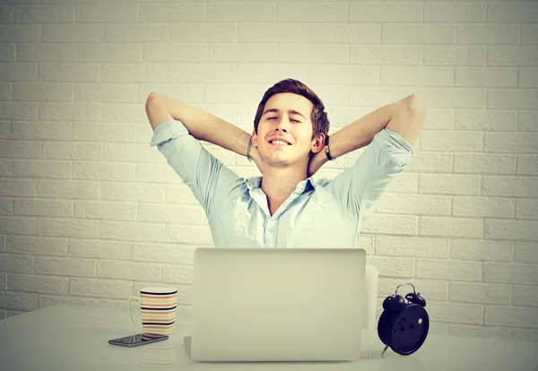 Relaxed man with laptop sitting at desk brick wall background