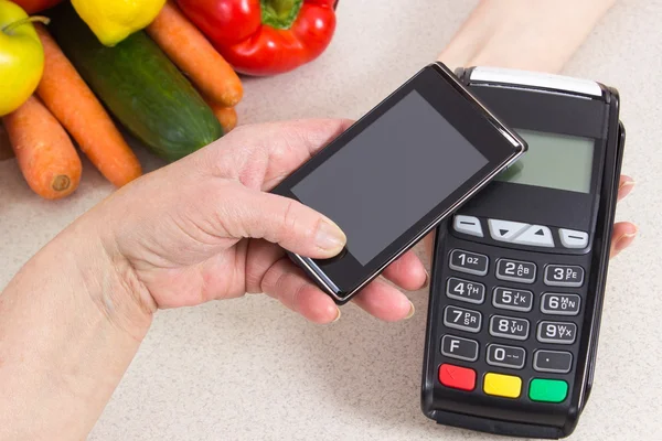 Hand of senior woman using payment terminal with mobile phone, paying for shopping