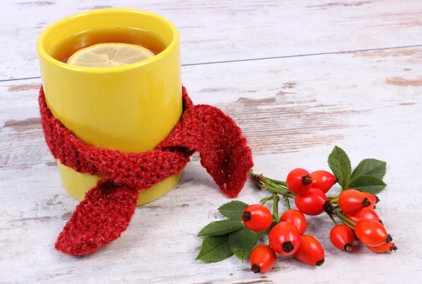 Cup of tea with lemon wrapped woolen scarf, warming beverage for flu, autumn decoration