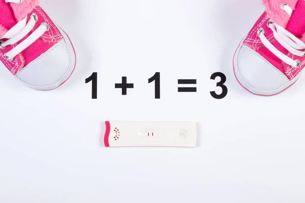 Pregnancy test with positive result and baby shoes on white background, expecting for baby
