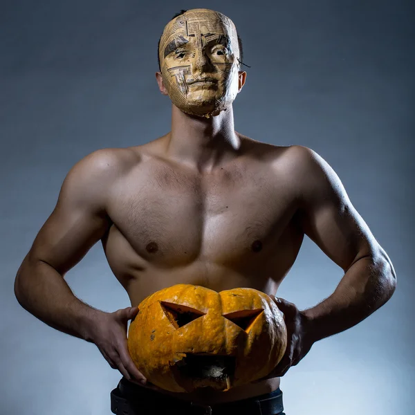 Muscular man in mask with pumpkin