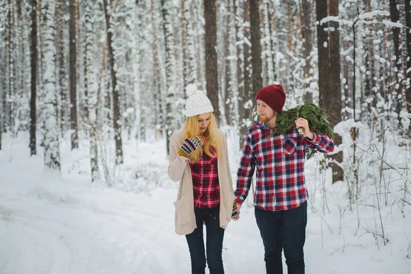 Young couple with fir twigs walk in the winter woods