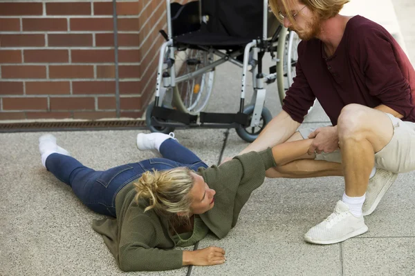 Disabled woman on pavement next to wheelchair getting help