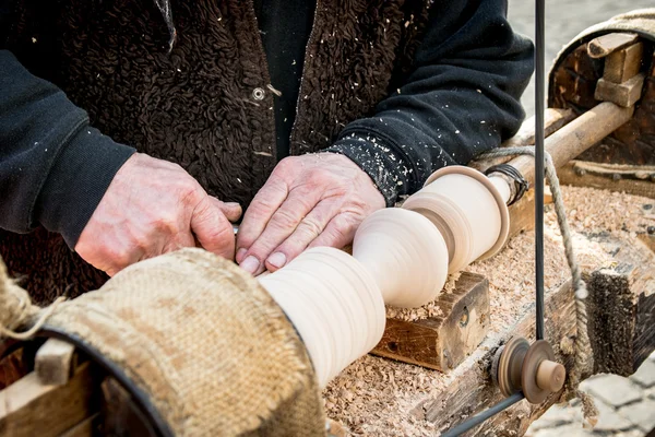 An artisan carves a piece of wood using a manual lathe.