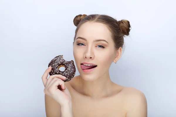 Portrait of a young woman with funny hairstyle and bare shoulders act the ape against white studio background with chocolate donut