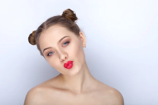 Portrait of a young pretty woman with trendy makeup bright red lips funny bun hairstyle and bare shoulders act the ape against white studio background