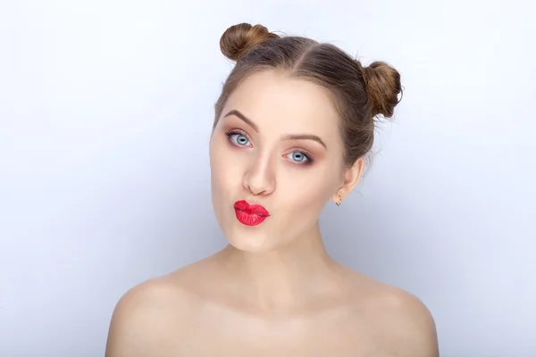 Portrait of a young pretty woman with trendy makeup bright red lips funny bun hairstyle and bare shoulders act the ape against white studio background