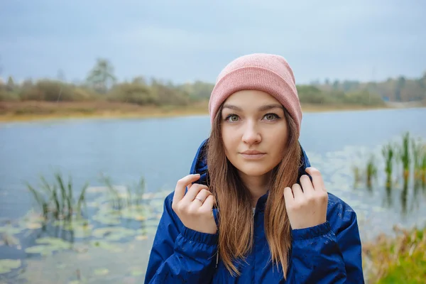 Stylish sporty brunette woman in trendy urban outwear posing in rainy autumn weather on the river bank. Vintage filter film saturated color. Fall mood and journey concept.