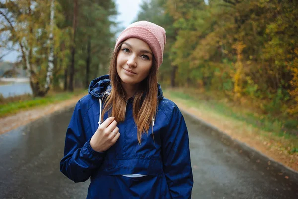 Stylish sporty brunette woman in trendy urban outwear posing in rainy autumn weather on the outdoors road. Vintage filter film saturated color. Fall mood and journey concept.