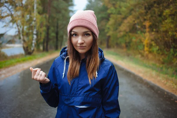 Stylish sporty brunette woman in trendy urban outwear posing in rainy autumn weather on the outdoors road. Vintage filter film saturated color. Fall mood and journey concept.