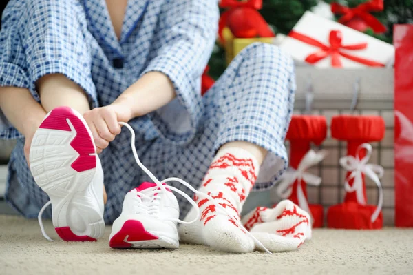 Woman in pajamas ties the laces of athletic shoes.