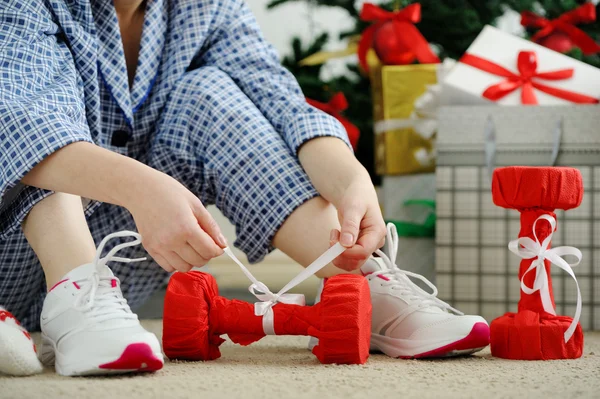 Woman in pajamas and athletic shoes unties the bow on the dumbbe