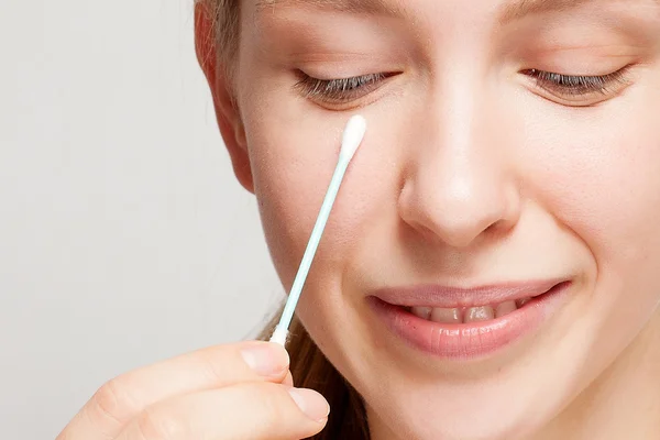 Happy beautiful young woman cleaning skin by cotton swab.