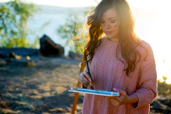 Young artist draws a seascape at sunset