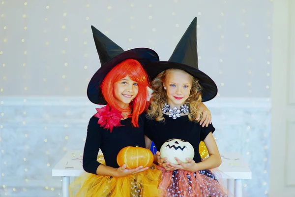 Two little girls in witch costume playing with pumpkins
