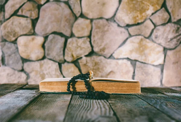 Prayer beads with a cross on an open old book on old wooden table on a background of stone walls. selective focus, toning photo. with space for your text