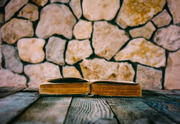 Old open book on old wooden table on a background of stone walls. selective focus, toning photo. with space for your text