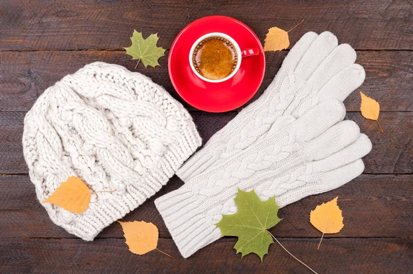 Coffee cup, gloves, handmade knitted hat and autumn leaves on wooden boards. Autumn background. Concept cozy autumn atmosphere with a cup of coffee