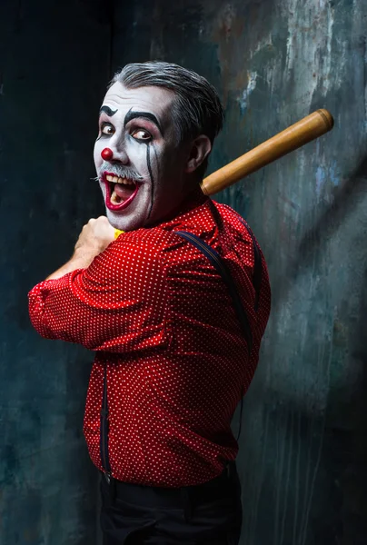 The scary clown and baseball-bat on dack background. Halloween concept