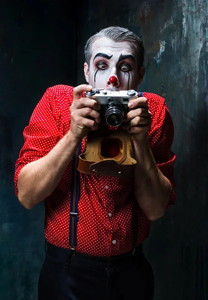 The scary clown and a camera on dack background. Halloween concept