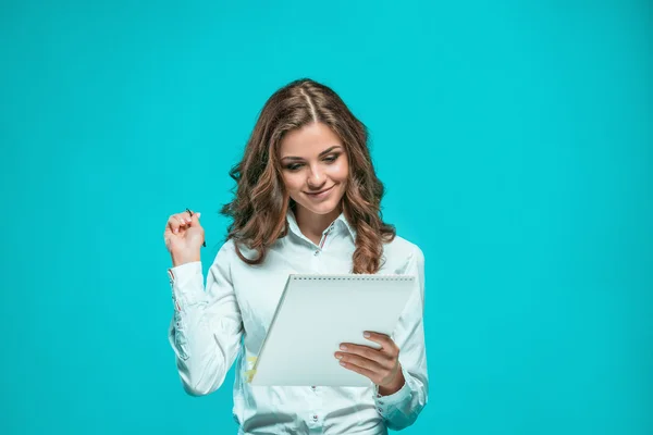 The smiling young business woman with pen and tablet for notes on blue background