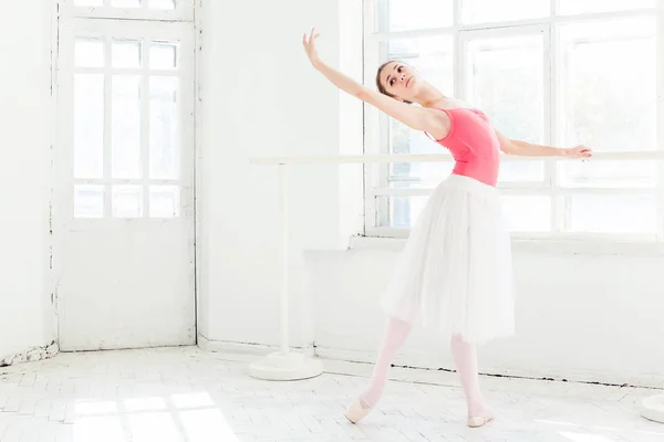 Ballerina posing in pointe shoes at white wooden pavilion