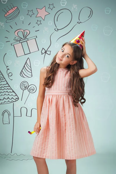 The cute cheerful little girl with festive cap on gray background