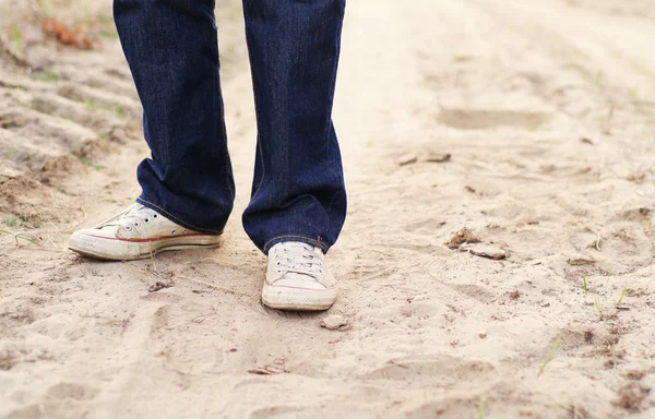 Male legs in blue jeans and gym shoes on the sandy dusty road