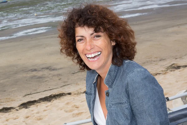 Brunette woman with curly hair laughing at beach