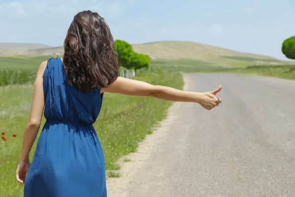 Woman hitchhiking on natural road.