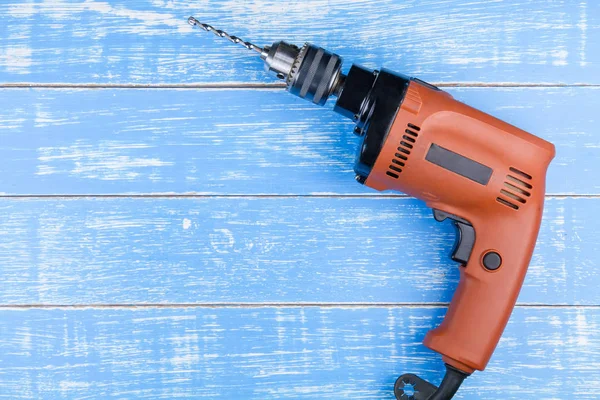 Electric drill with a drill on blue wooden table background copy