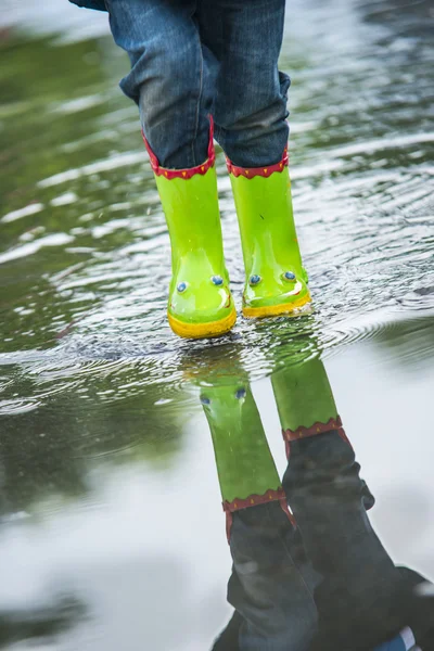 Baby in green rubber boots walking on puddle