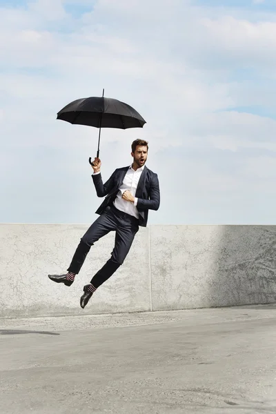 Handsome businessman jumping with umbrella