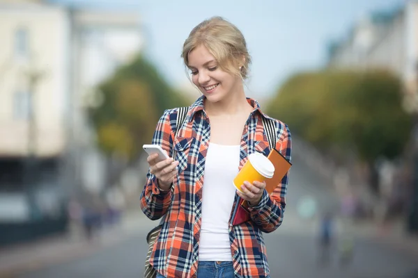 Portrait of attractive student girl against street, looking at phone