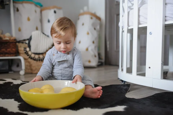 Cute happy baby boy eating cookies at home and playing with plate of lemons. Lifestyle indoor capture in cozy modern interior