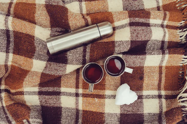 Winter picnic on the snow. Hot tea, thermos and snowball heart on cozy warm blanket. Outdoor seasonal activities.
