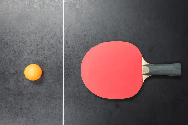 Table tennis racket with orange ball on black