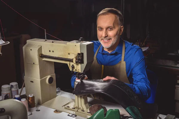 Happy shoemaker sitting at the sewing machine