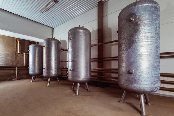 Steel storage tanks arranged in row indoors at wall background.