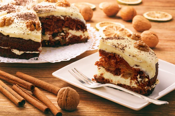 Piece of carrot cake with cheese cream on brown background.